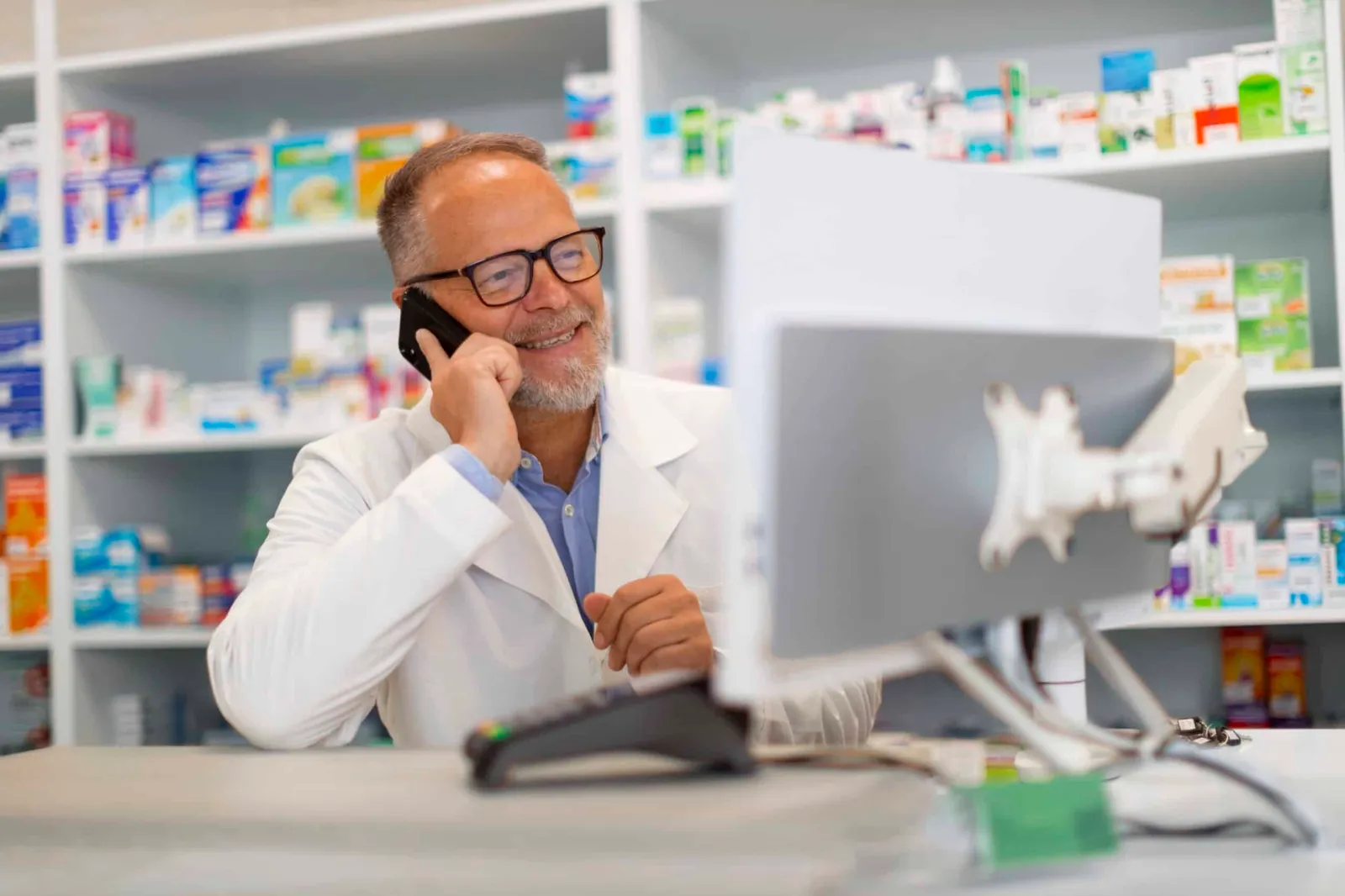 A community pharmacist on the phone at his pharmacy counter